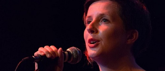 Close up of a woman singing into a mike, dark background and red light on face