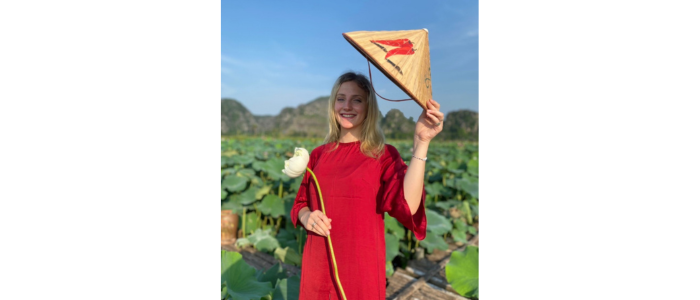 Young woman wearing a red dress and carrying a white flower and traditional Vietnamese hat