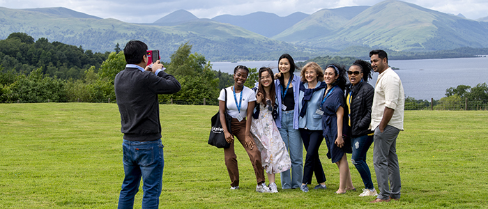 Students standing for a group photo on a grassy slow with views of the hills and the sea at Dumfries