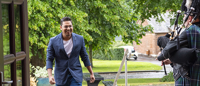 A student walking up stairs to enter a building with someone playing the bag pipes at the door