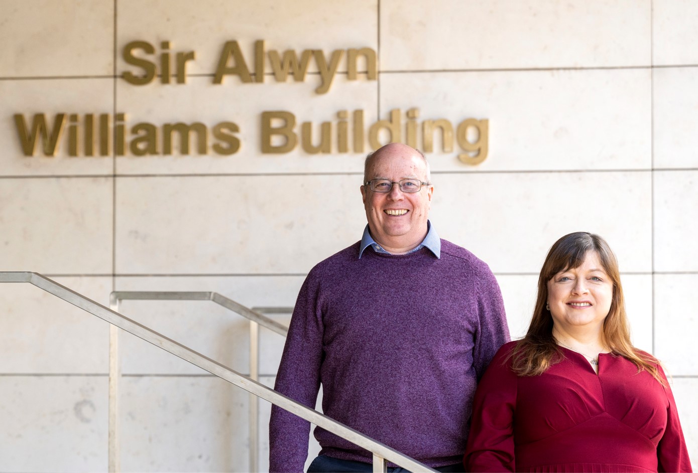 A man and woman standing on an internal stair case talking in a modern building, with a logo included