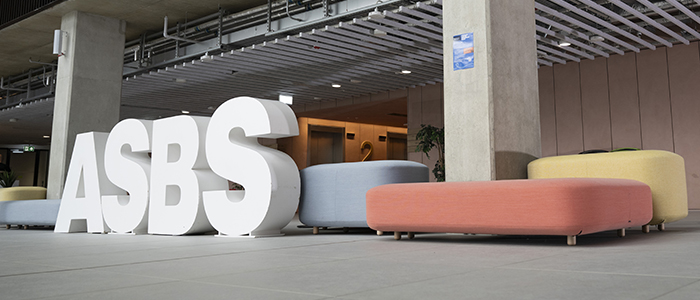 Students in the atrium of the Adam Smith Business School & Postgraduate Taught Hub walking by large ASBS letters