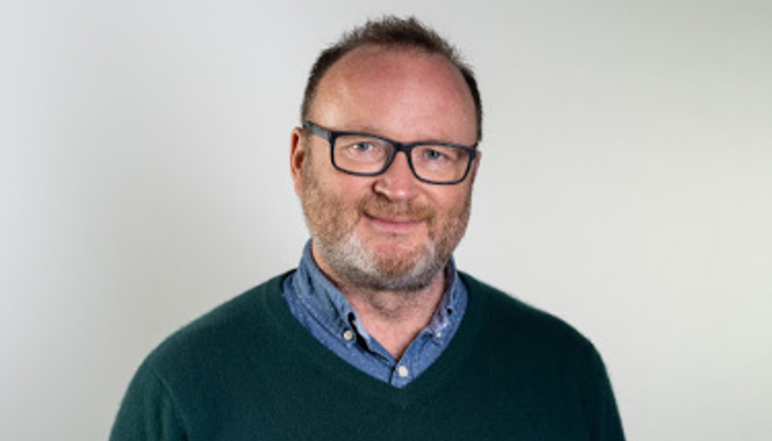A head and shoulders profile shot of Professor Mike Barrett stood in front of a plain, white background