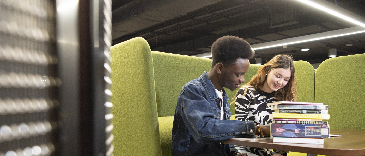 Two students sitting at table with a pile of books