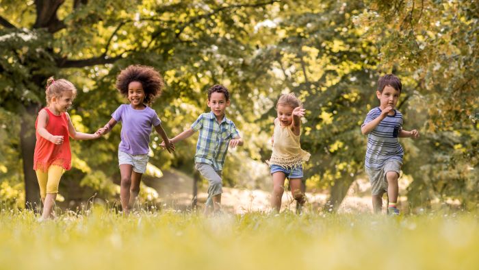A group of boys and girls running across grass on a sunny day.