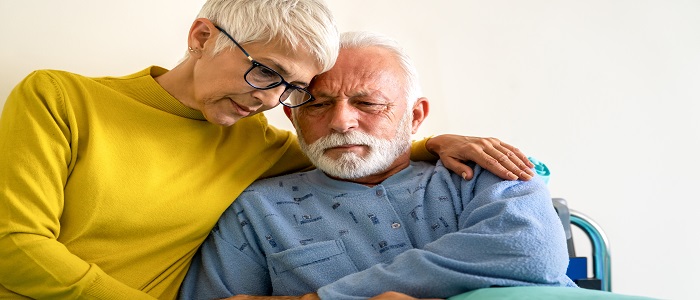 Elderly couple hold each other and look sad