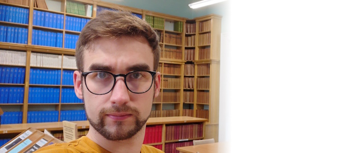 Joshua Sharkey in front of library shelves stocked with journals.