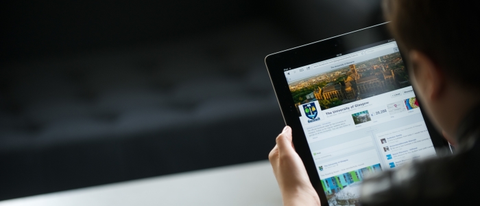 An over the shoulder view of an individual reading the University of Glasgow homepage on their tablet
