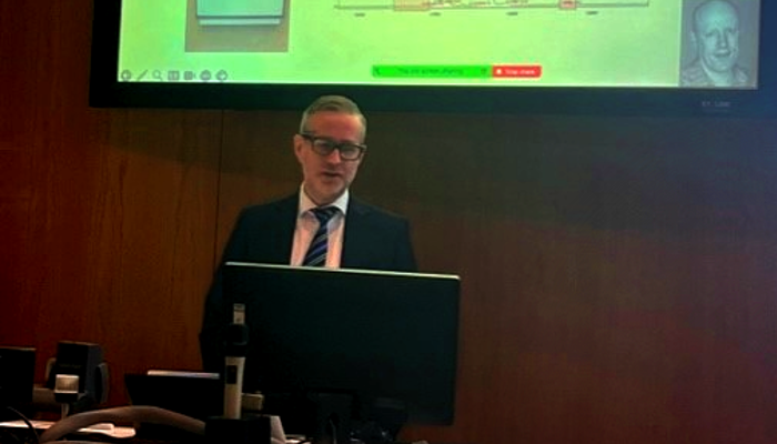 Professor Robert Gray stood at a podium as he delivers his inaugural lecture with a slide visible on the large screen above his head