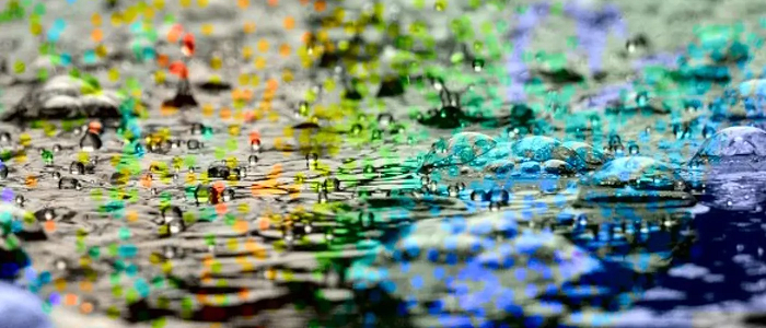 Water droplets landing on water with rainbow reflection