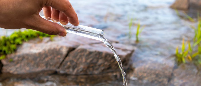 Hand pouring test tube of water into stream