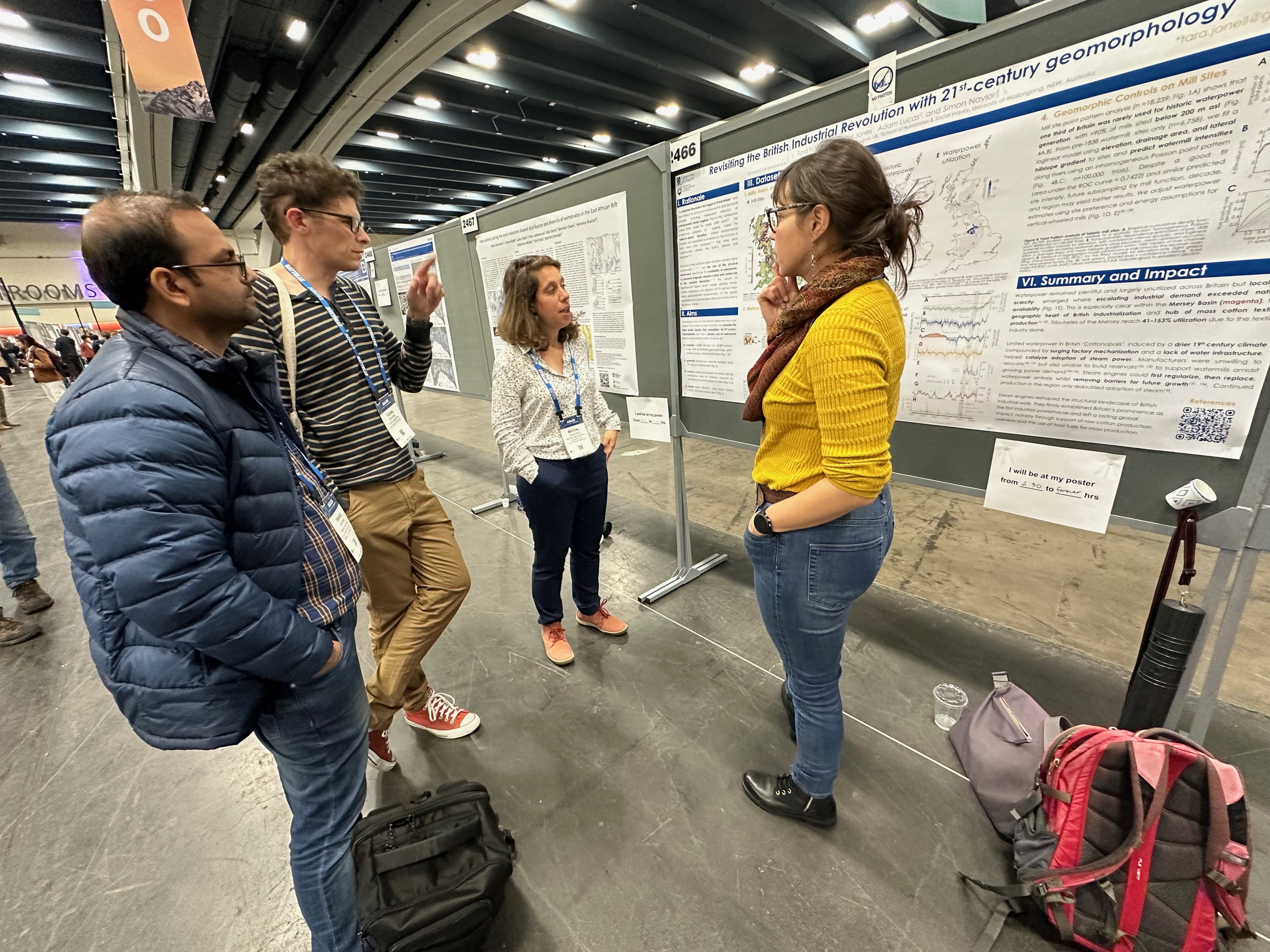 Woman in yellow jumper standing in front of poster with other people asking questions