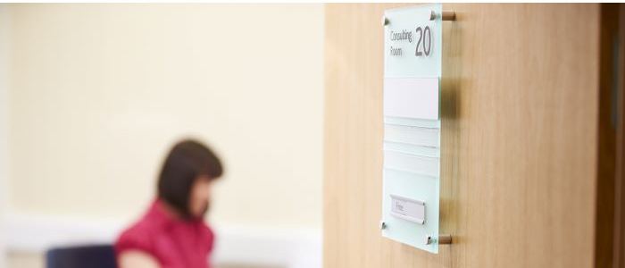 A GP is at a desk with the consultation room door open