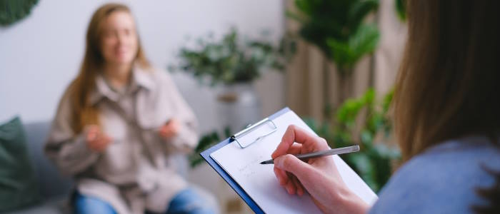 A person at an occupational health review talking to the practitioner who is taking notes on a clipboard.