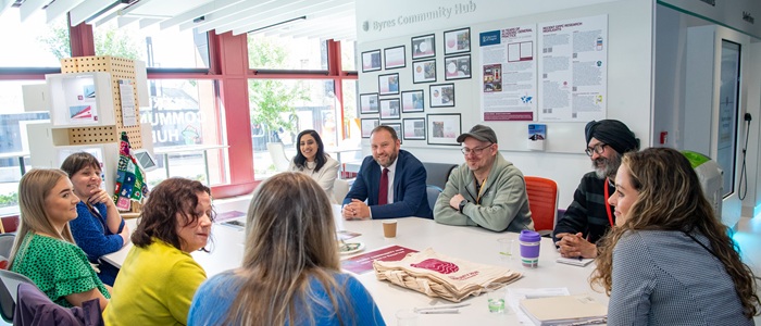 A group of people sitting around the table in Byres Hub with an exhibition wall behind them