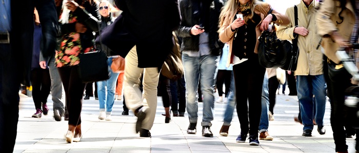 Men and women walking on street. The photo is taken from street level. Two people are checking their mobile phones