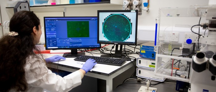 Researcher in lab coat and blue gloves using computer