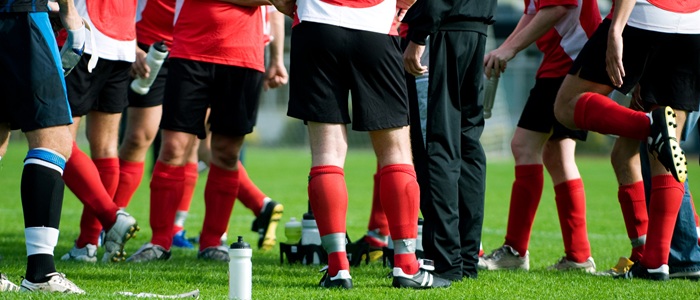 Footballers wearing red and white tops, red socks and black shorts are standing in a group on the pitch.