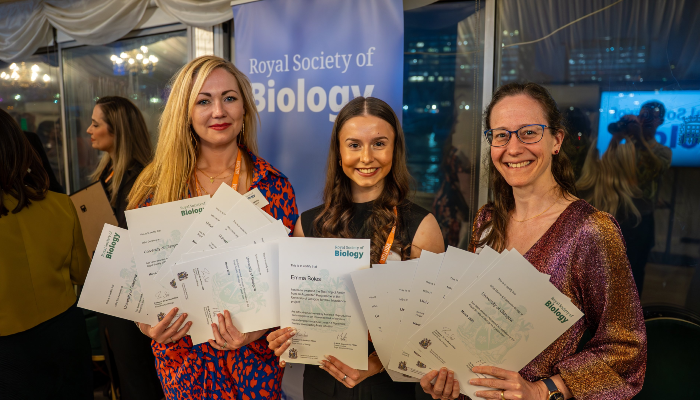 Dr Laura McCaughey, hons student Emma Boles, and Dr Anna McGregor stood in front of the RSB logo on a pull-up stand at the RSB ceremony. The trio are each holding certificates of the 16 accredited degrees
