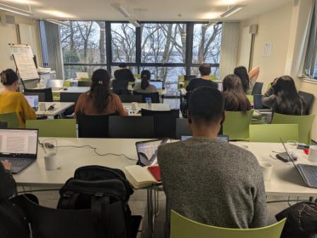 Writing retreat participants inside with laptops and notepads facing a window overlooking Loch Lomond
