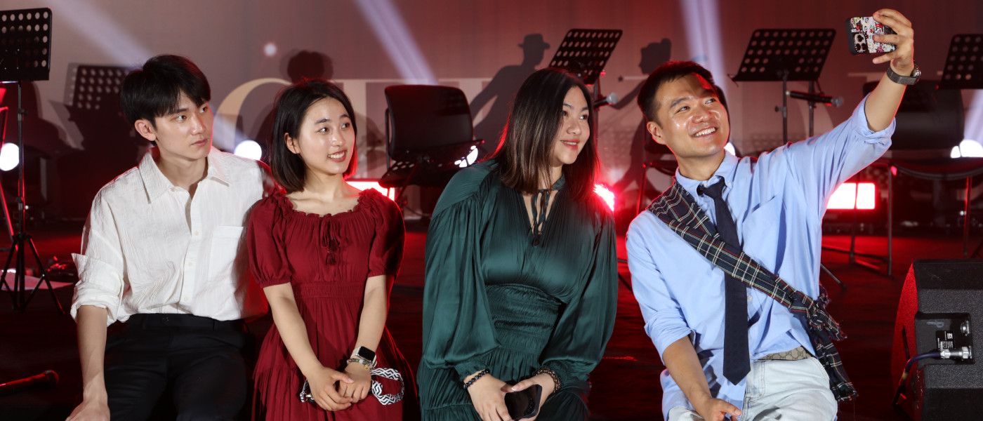 Two well dressed students sitting with two staff members, smiling at the camera