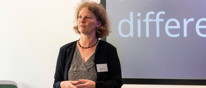Photo of Professor Petra Meier standing in front of a screen, listening at a workshop