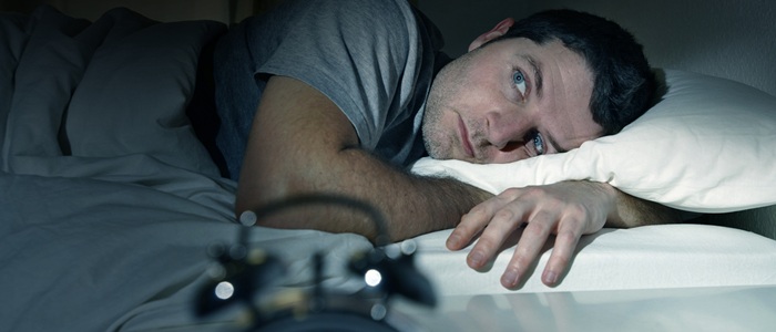 Man lying awake in bed with an alarm clock in the foreground
