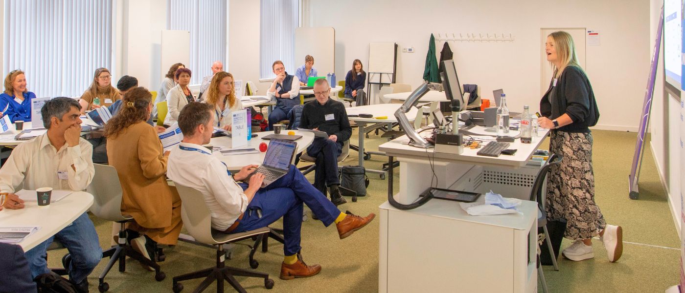 A woman presenting in front of a group of people sitting around tables