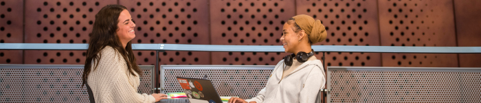 Students chatting at a table in the JMS with a laptop