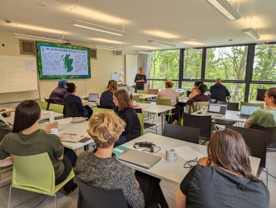 People sitting in table groups in a room looking towards a screen