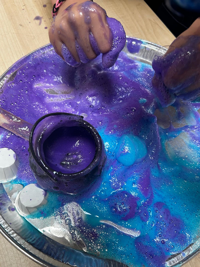 Child's hands covered in foaming purple and blue paint