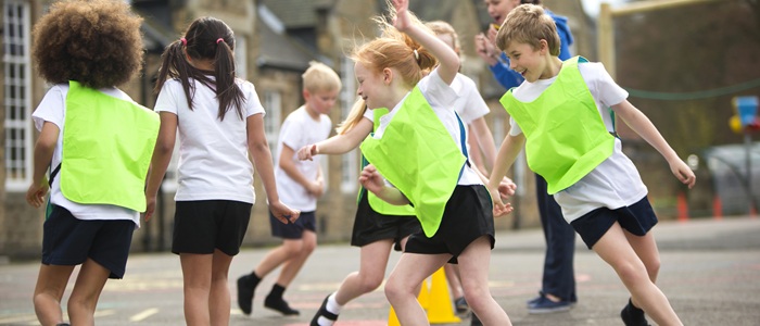 Children running around cones in a school playground. Some children are wearing hi-vis vests.