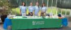 Four researchers wearing blue Glasgow Science Festival t-shirts standing behind a table. The green tablecloth has the University of Glasgow logo on it.