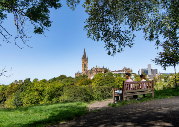 Students sitting on a bench overlooking the Gilbert Scott Building for Kelvingrove Park