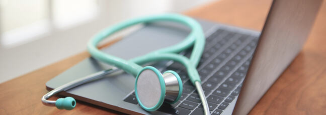 A green stethoscope sits on top of a laptop