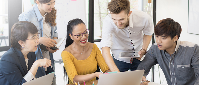 Group of five people looking at laptops and collaborating