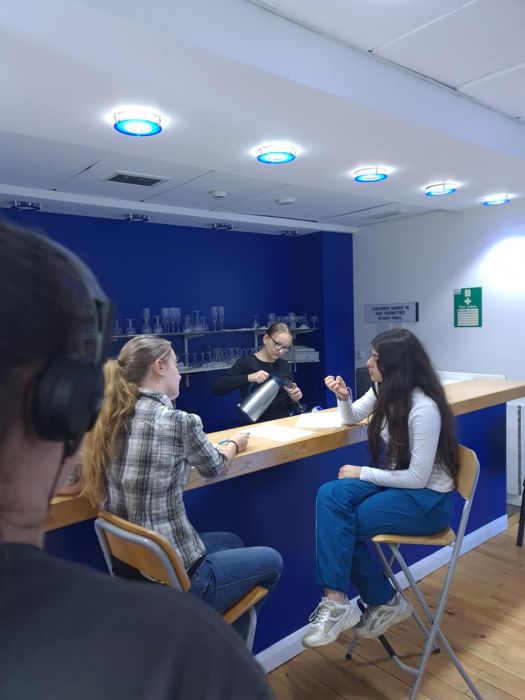 Two people sitting together while one person pours a drink in Gilmorehill Halls