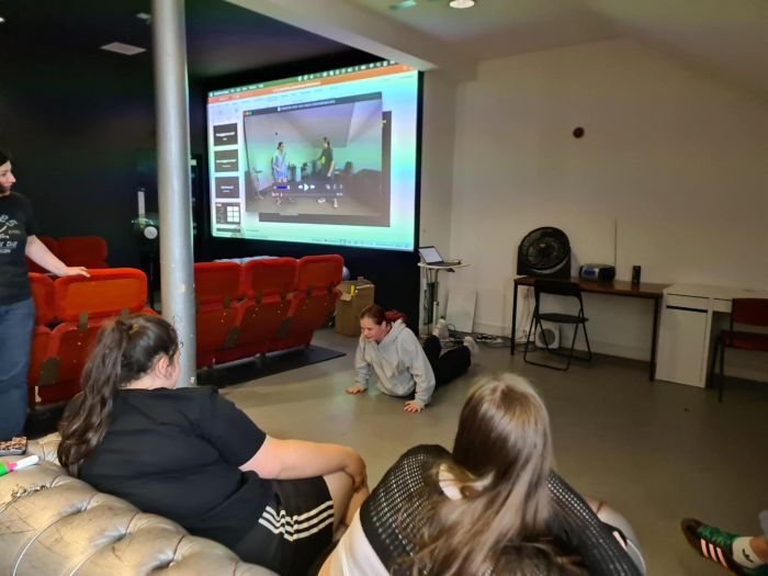 Two people sitting watch a young person on the ground pushing themself up