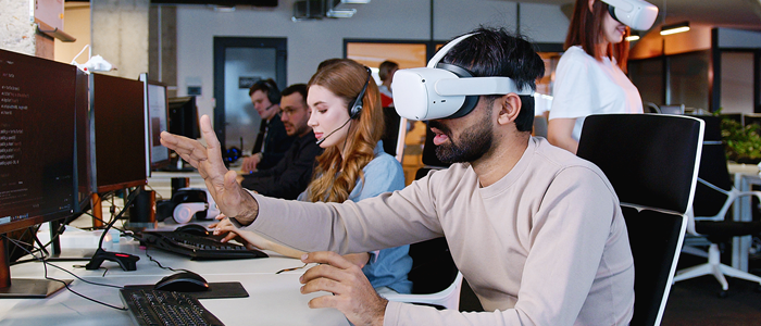 Student wearing VR headset and sitting in front of a desktop computer screen