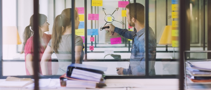 Staff looking at a clear board with colourful post-it notes on it
