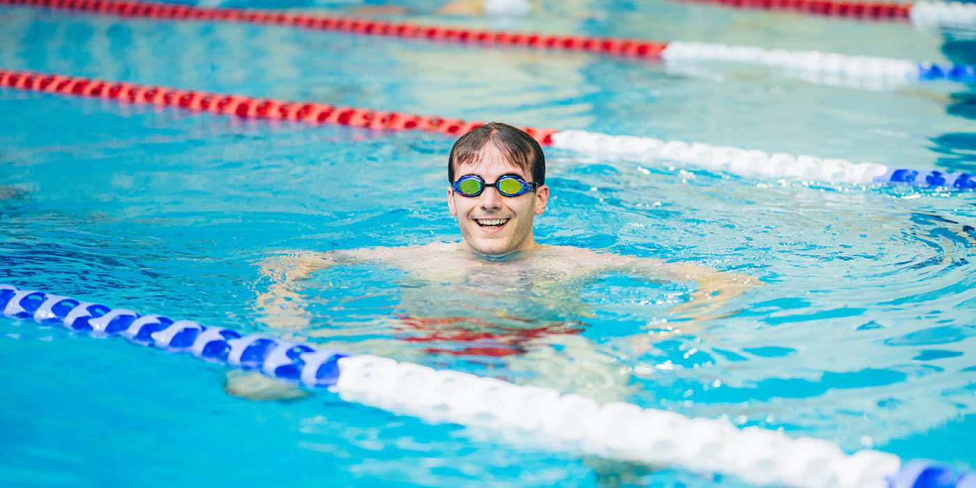 Male student swimming in the pool, looking and smiling at the camera.