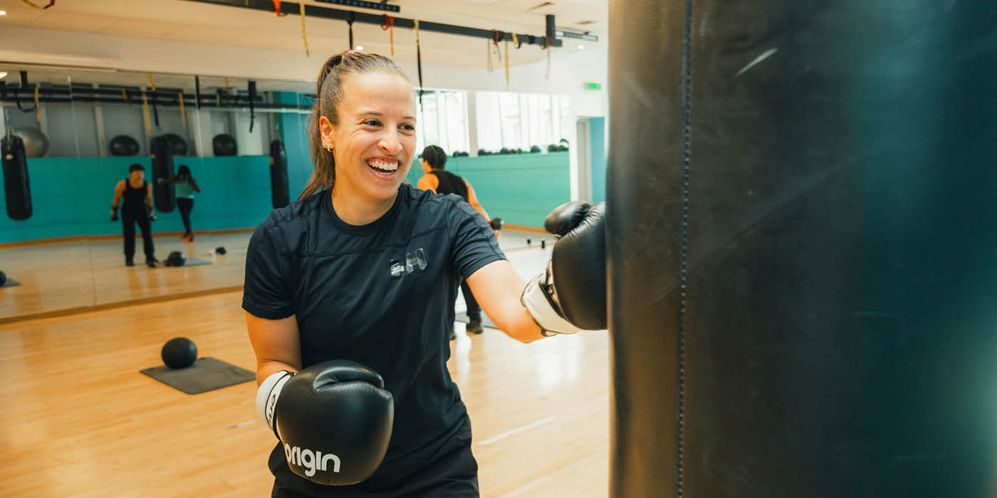 Female student smiling and punching boxing bag in a UofG Sport studio