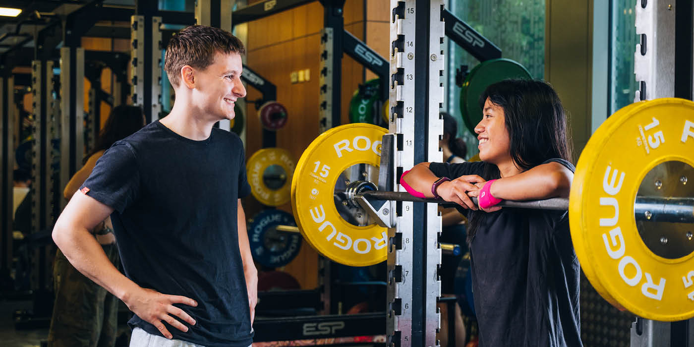 Male and Female student speaking whilst at a squat rack in the gym