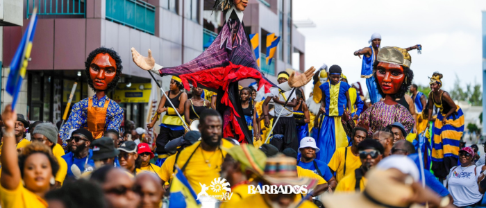 A crowd of people wearing blue and yellow holding puppets as they walk through a street