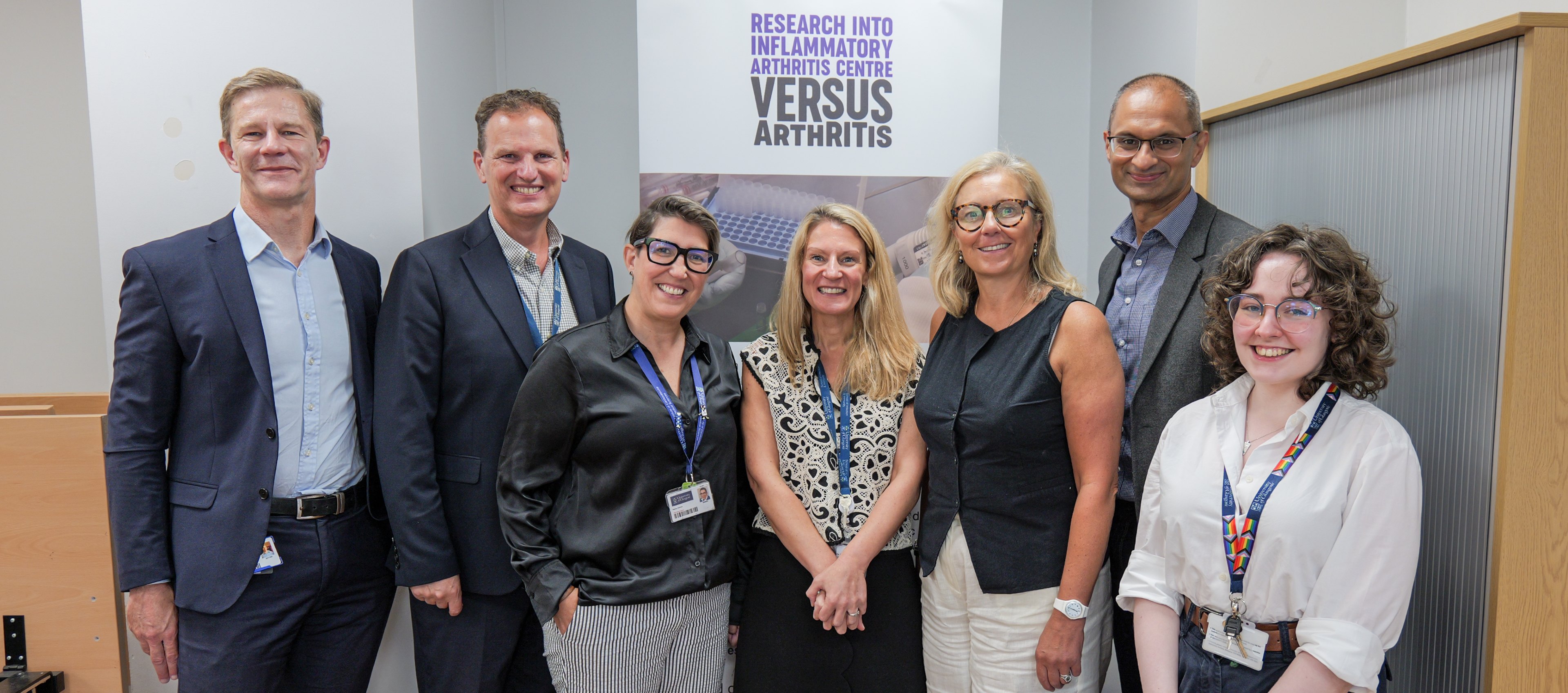 Staff stood with Rachael Hamilton in front of a Versus Arthritis pull-up banner. From left to right: Stefan Siebert, Iain McInnes, Carmen Huesa, Eve Smith, Rachael Hamilton MSP, Neil Basu, and Hope Conway-Gebbie.