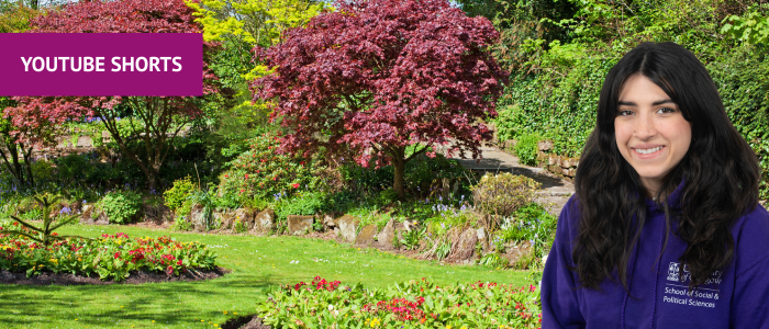 Victoria Peak in Glasgow, picture shows a green lawn with flower beds filled with yellow and red flowers, a path going up to the right and a line of trees with yellow and red leves. In the top left-hand corner there is a pink box with 'YouTube Shorts' written in it and on the right-hand side there is a headshot of a smiling woman wearing a purple hoodie.