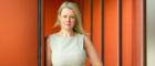 Professor Deborah Cairns wearing a light sleeveless dress standing against an orange background