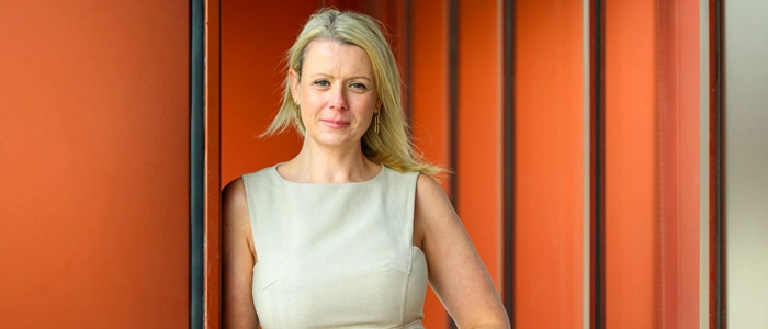 Professor Deborah Cairns wearing a light sleeveless dress standing against an orange background