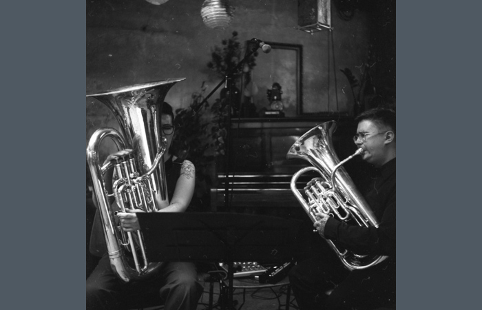 Picture shows two musicians sitting next to each other playing brass instruments