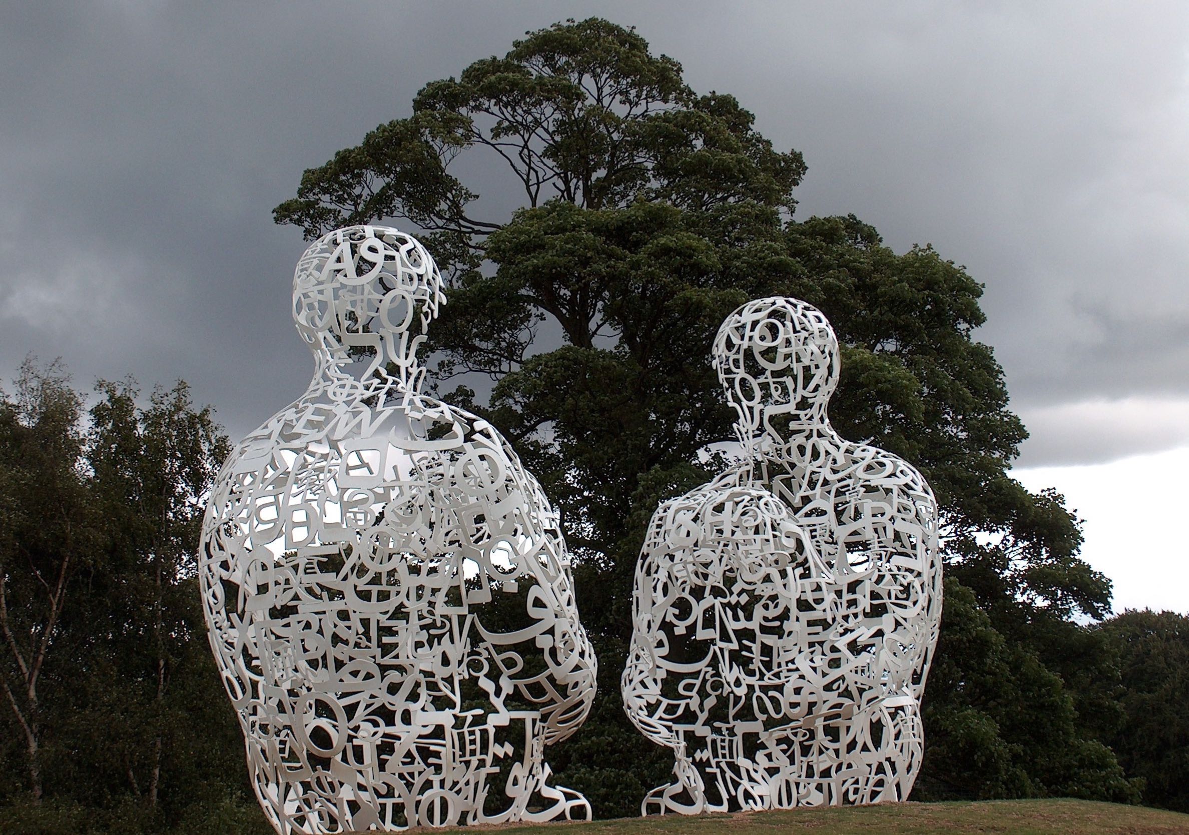 Two sculpted human figures made of letters sitting under a tree